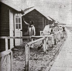 Black-and-white photo showing painters at work painting the vintage St Annes Beach Huts along the seaside