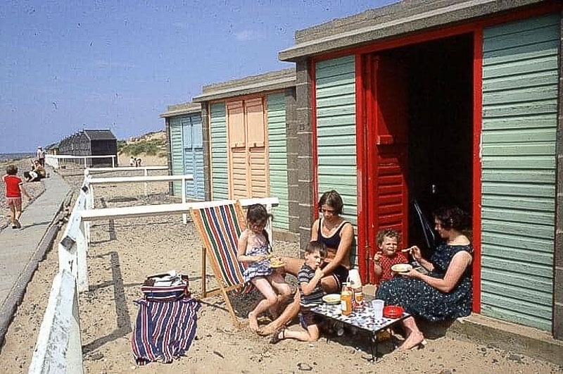 A family picnic beside the green beach huts