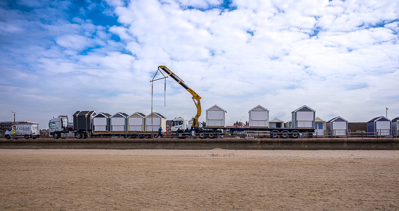 A crane lowering a modern beach hut into position