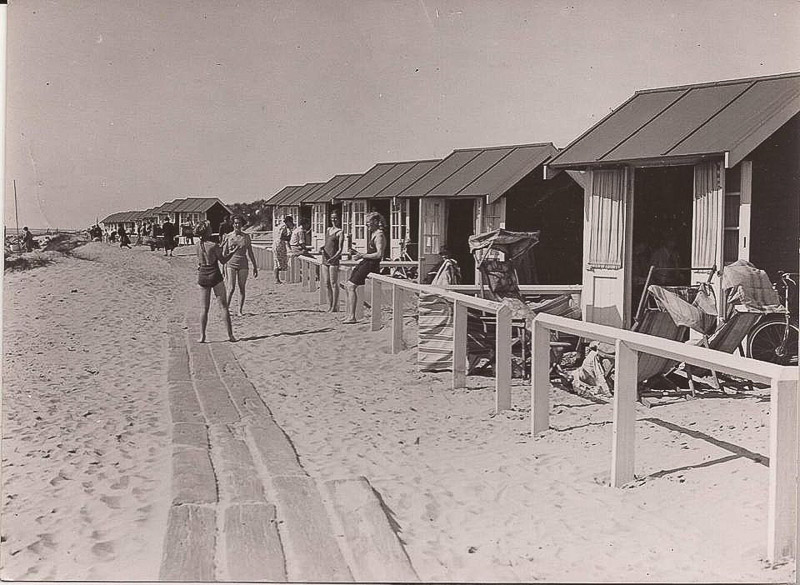 A historic photograph of visitors beside a row of beach huts